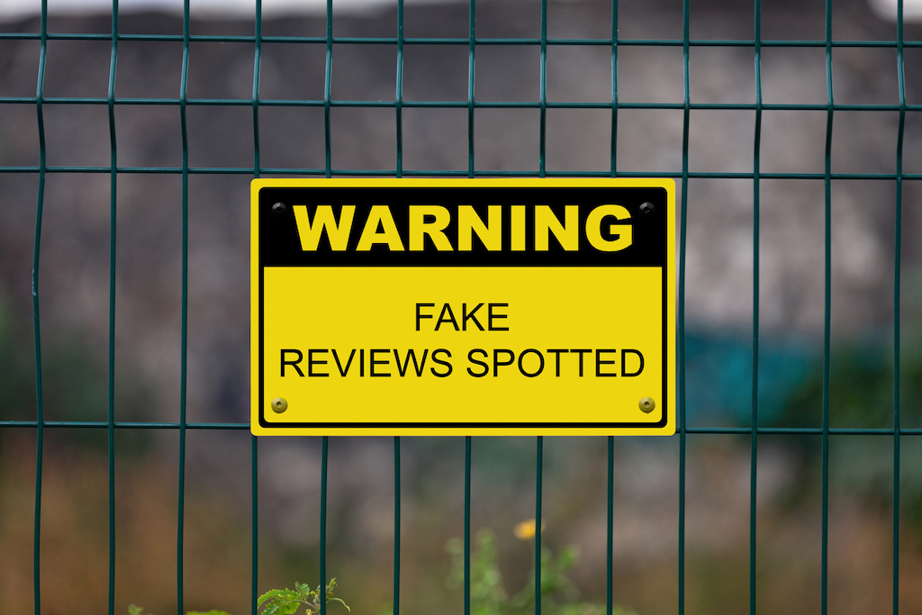 Yellow warning sign on a fence stating : Fake Reviews