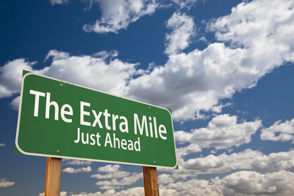 The Extra Mile Just Ahead green sign over clouds and blue sky